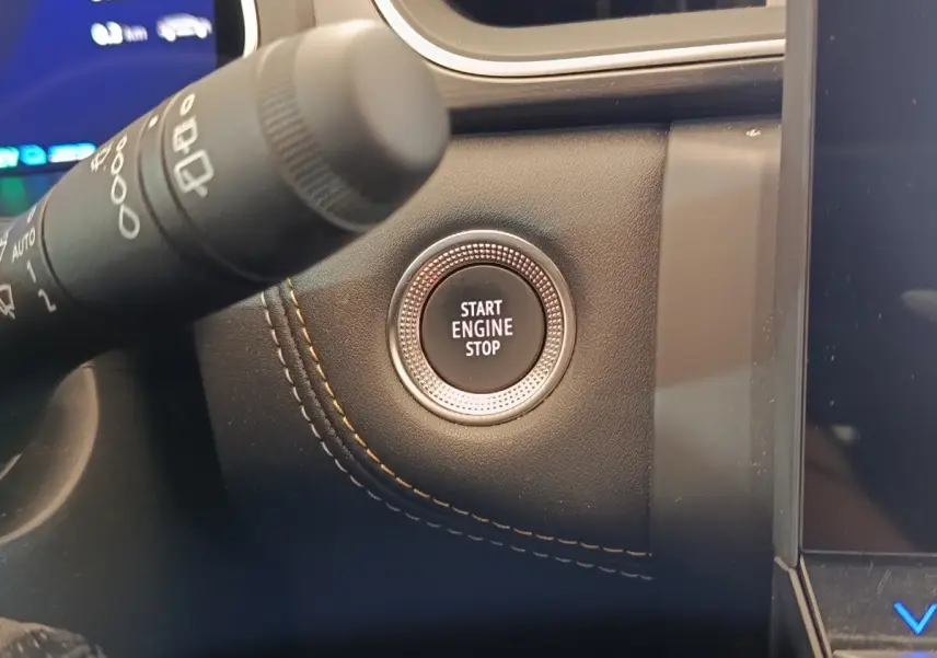 Gros plan sur le bouton Start Engine Stop entouré de cuir noir avec surpiqûres orange dans le tableau de bord Renault Symbioz.