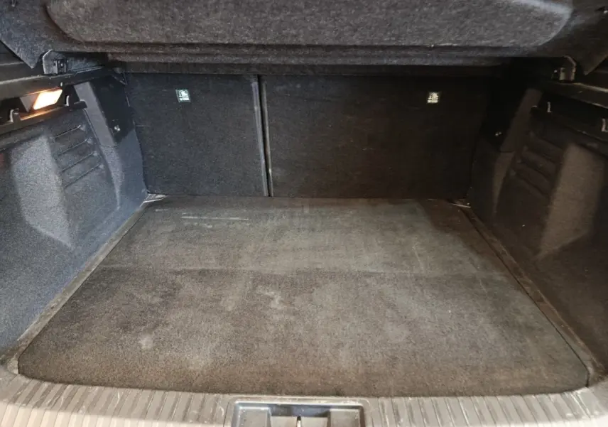 Coffre spacieux noir vu de l'intérieur, avec banquette arrière rabattue et éclairage latéral à gauche.