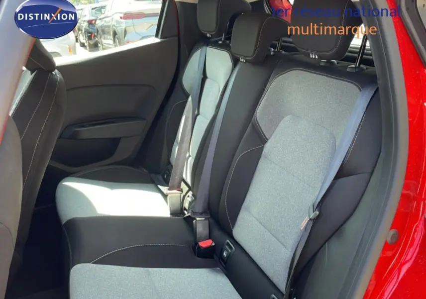 Vue intérieure de la banquette arrière d'une Renault Clio rouge flamme métal, sièges tissu gris et noir avec ceintures visibles.