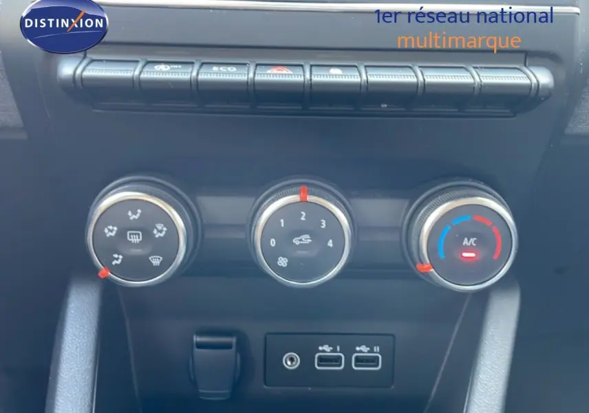 Gros plan sur les commandes de climatisation et ventilation de la Renault Clio rouge flamme, avec boutons rotatifs et ports USB.