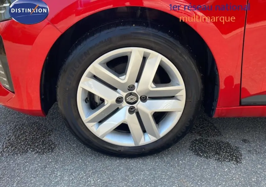 Gros plan sur la roue avant droite d'une Renault Clio rouge flamme métal, mettant en valeur la jante alliage moderne.
