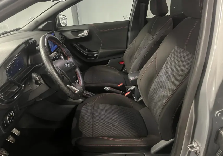 Intérieur avant droit du Ford Puma gris, sièges tissu noir avec surpiqûres rouges et volant ST-Line à méplat.