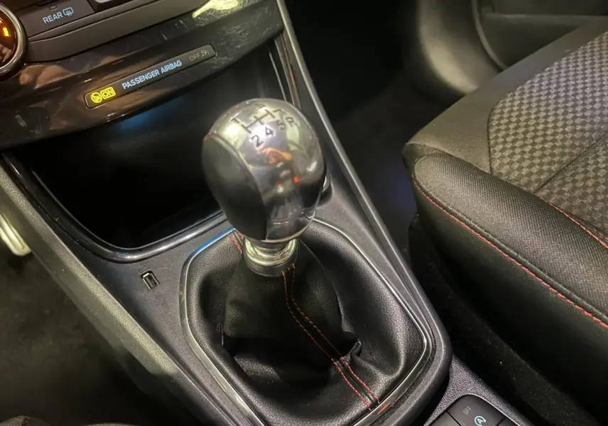 Levier de vitesses manuel gainé de cuir noir avec surpiqûres rouges dans l'habitacle du Ford Puma gris.