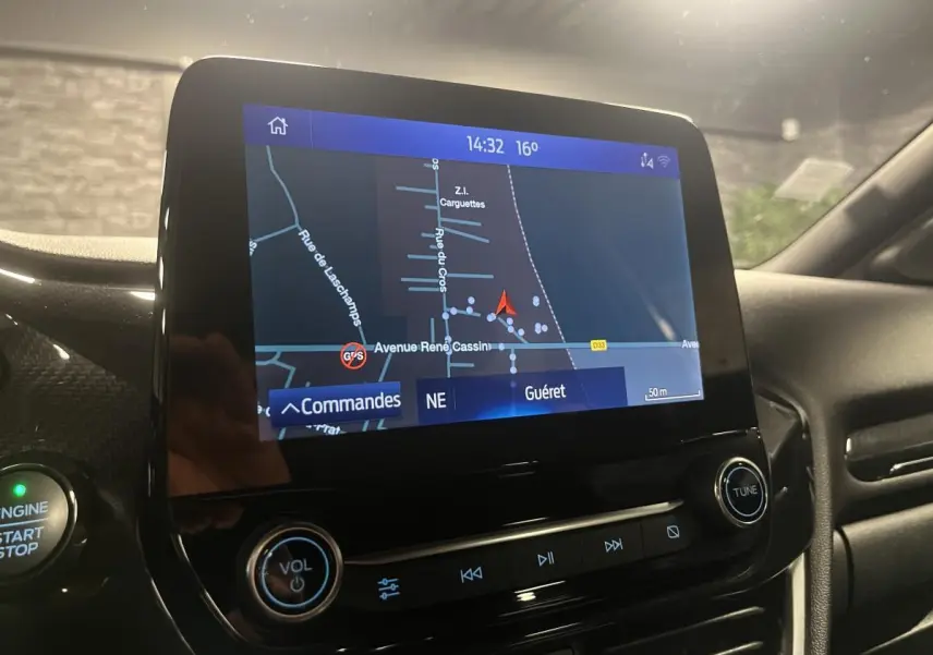 Écran tactile central du Ford Puma gris, affichant la navigation GPS avec commandes audio et bouton démarrage visible.