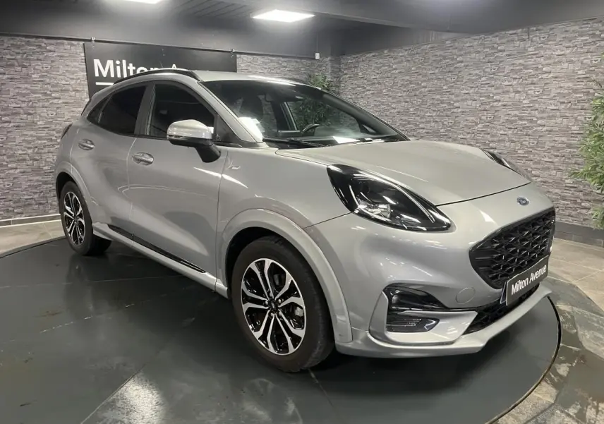 Ford Puma gris métallisé en 3/4 avant droit avec jantes alliage noires et barres de toit noires visibles