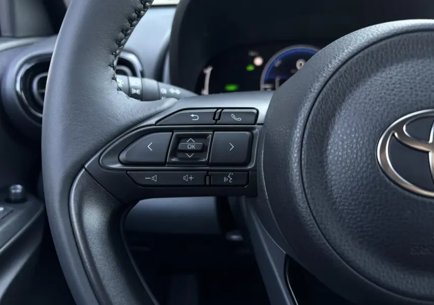 Gros plan sur le côté gauche du volant cuir noir de la Toyota Yaris 2025, avec commandes multifonctions intégrées.
