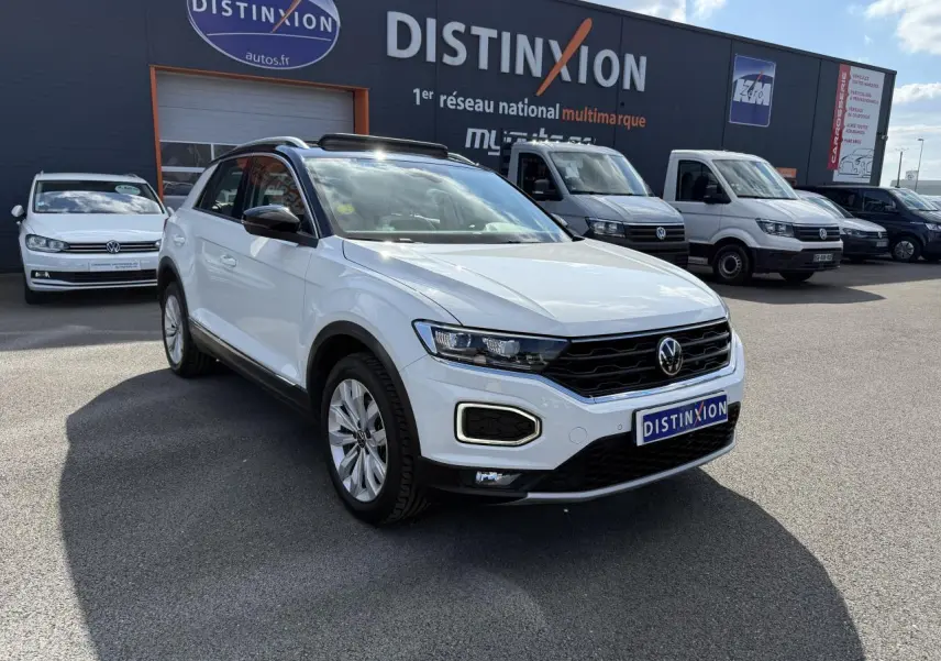 Volkswagen T-Roc blanc en 3/4 avant droit, avec toit ouvrant en verre et calandre noire distinctive.