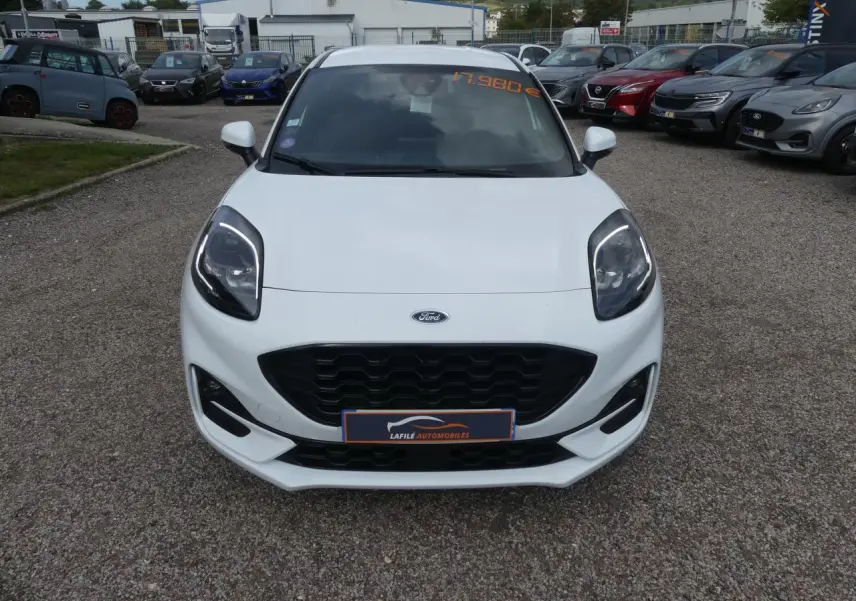 Vue avant d'une Ford Puma blanche ST Line avec calandre noire et phares LED, sur un parking extérieur.