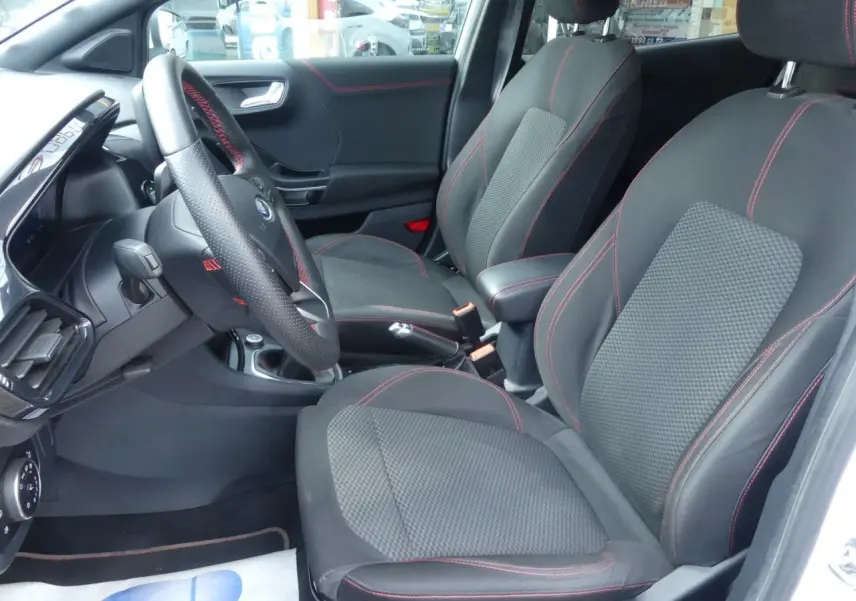 Intérieur avant droit du Ford Puma blanc 2020 ST Line, sièges tissu noir avec surpiqûres rouges et volant méplat.