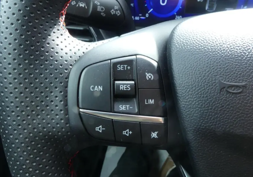 Gros plan sur les commandes de régulateur de vitesse et volume au volant perforé noir du Ford Puma blanc 2020.