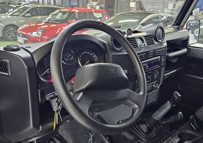 Vue intérieure côté conducteur du Land Rover Defender 110 Station Wagon gris de 2010, volant et tableau de bord visibles.