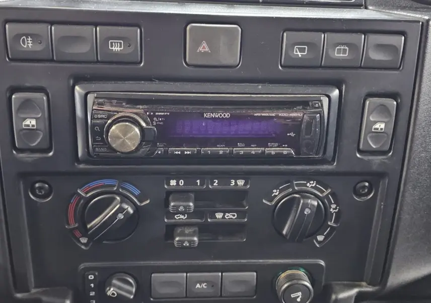 Tableau de bord du Land Rover Defender 110 II Station Wagon gris, montrant la radio Kenwood et les commandes de climatisation.