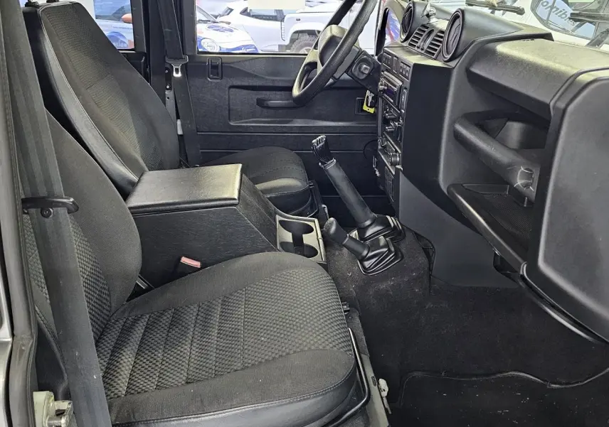 Intérieur du Land Rover Defender 110 Station Wagon gris, vue côté gauche sur les sièges avant et la boîte manuelle.