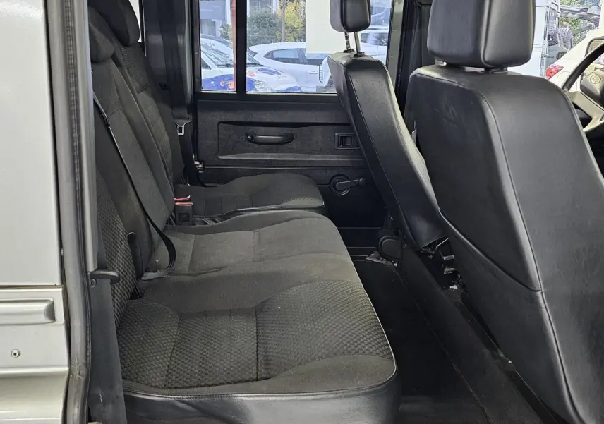 Vue intérieure côté gauche du Land Rover Defender 110 Station Wagon gris, montrant les sièges arrière et avant en tissu et cuir noir.