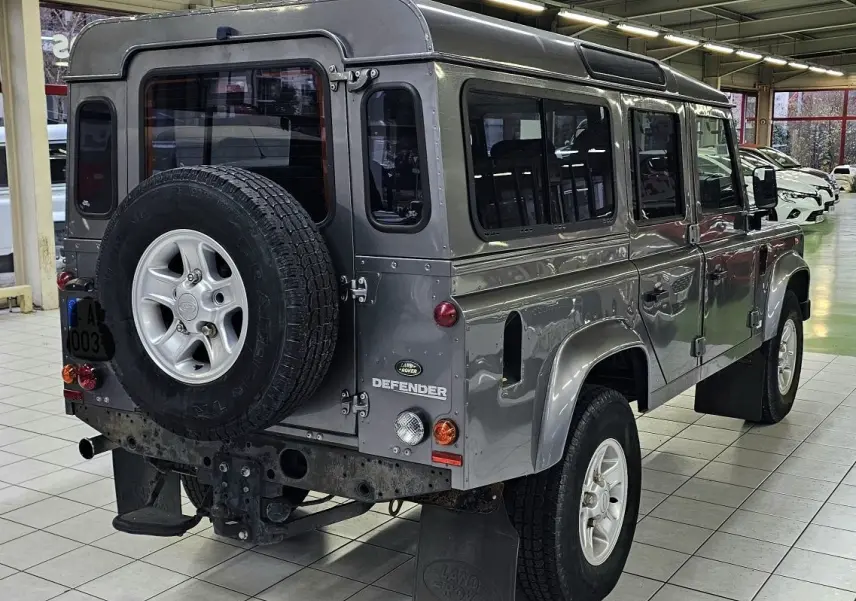 Vue 3/4 arrière droite d'un Land Rover Defender 110 Station Wagon S gris, avec roue de secours fixée à la porte arrière.