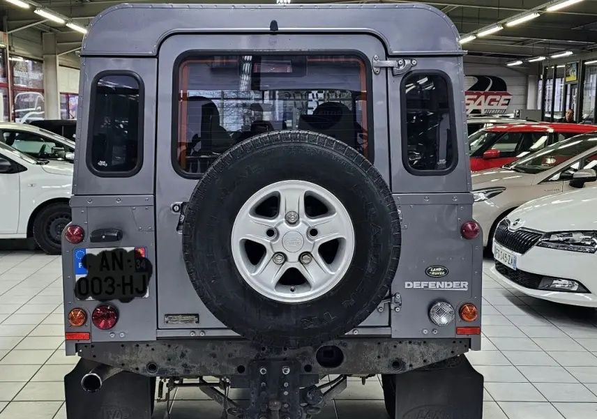 Vue arrière d'un Land Rover Defender 110 Station Wagon gris, avec roue de secours fixée sur la porte arrière.
