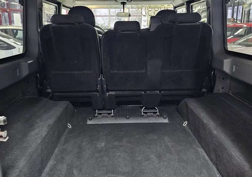 Vue arrière du Land Rover Defender 110 gris de 2010, montrant l'espace de chargement et les sièges noirs rabattus.