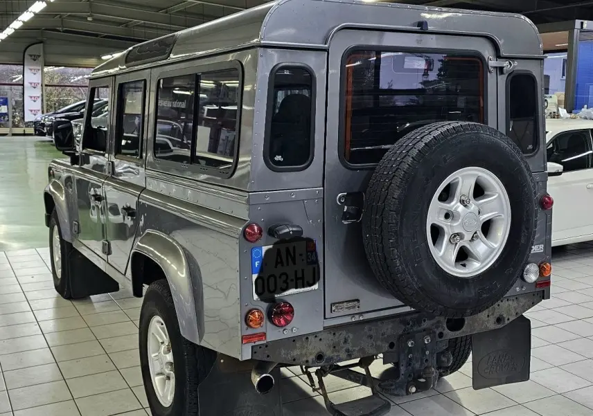Vue 3/4 arrière droite d'un Land Rover Defender 110 Station Wagon gris avec roue de secours fixée à la porte arrière.