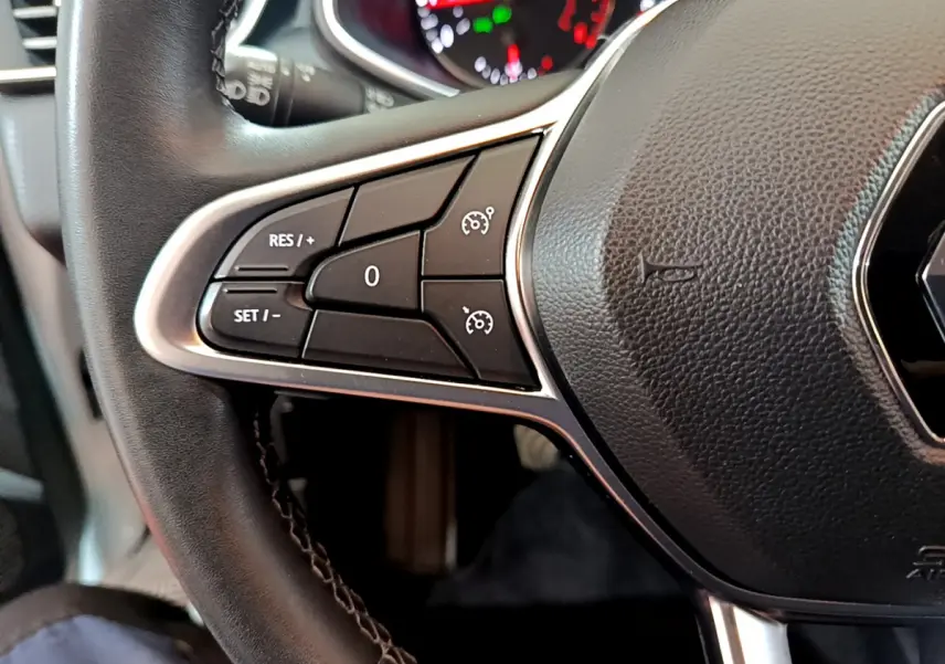 Gros plan sur la partie gauche du volant cuir noir de la Renault Clio Business blanche, avec commandes de régulateur de vitesse.