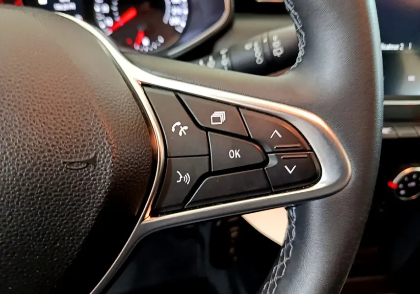 Gros plan sur le côté droit du volant cuir de la Renault Clio Business blanc, avec commandes multifonctions visibles.