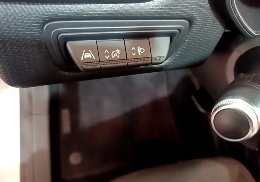 Gros plan sur les commandes de réglage d'assistance et phares dans l'habitacle noir de la Renault Clio Business blanche 2021.