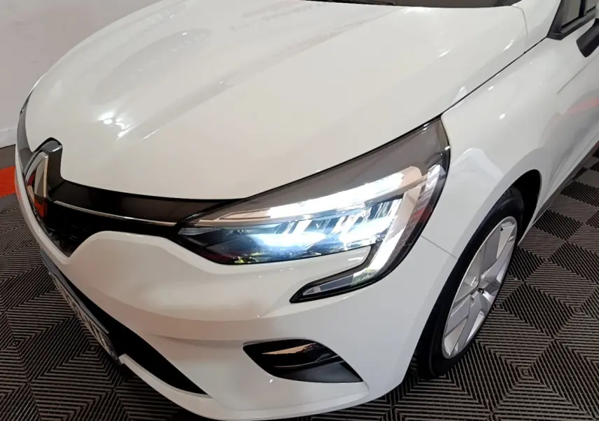 Vue 3/4 avant droit d'une Renault Clio Business blanche avec phares LED allumés et jantes modernes.