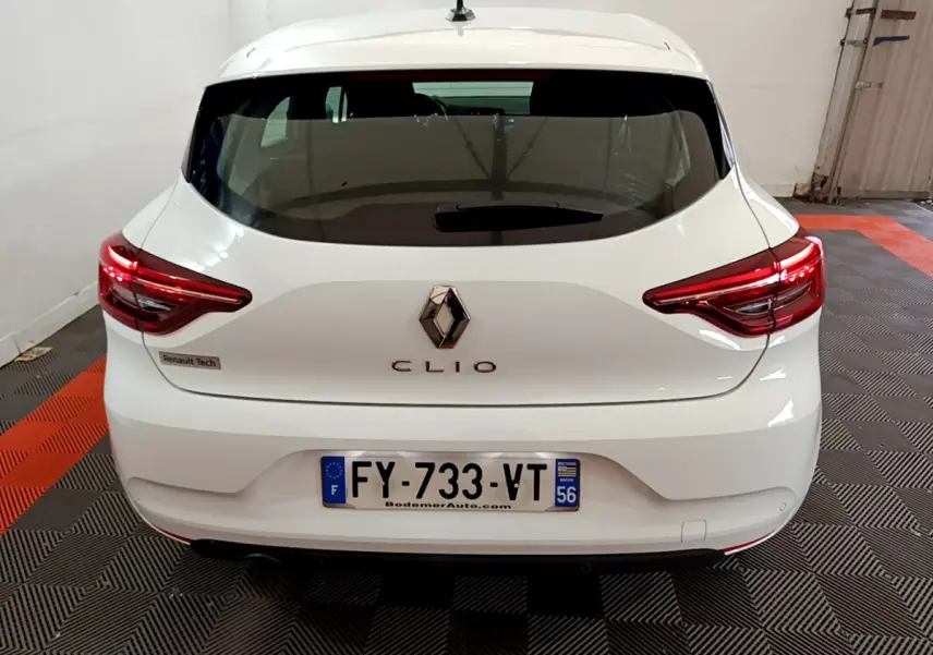 Vue arrière d'une Renault Clio blanche 2021 avec feux LED et logo centré sur un sol à damiers noir et orange.