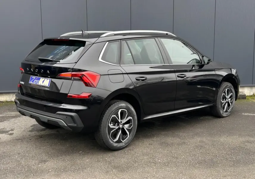 Vue 3/4 arrière droite d'un Skoda Kamiq noir Magic avec jantes alliage et barres de toit argentées.
