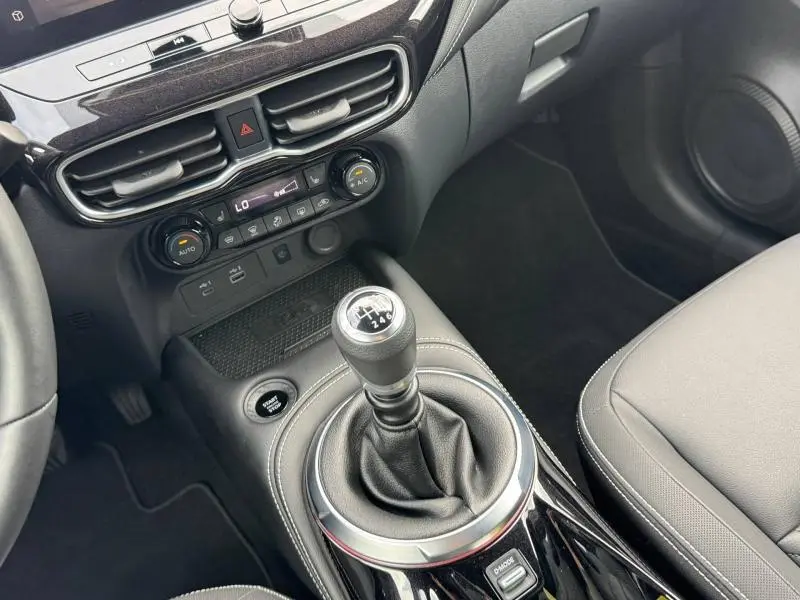 Vue intérieure centrée sur le levier de vitesses manuel noir du Nissan Juke Tekna 2025 avec console et commandes climatisation.
