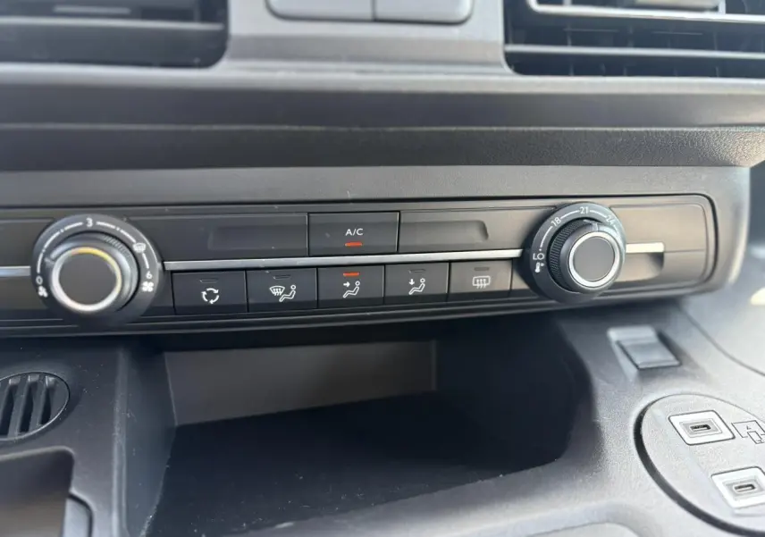Gros plan sur la console centrale noire du Citroën Berlingo ë-136 avec commandes de climatisation et prises USB visibles.
