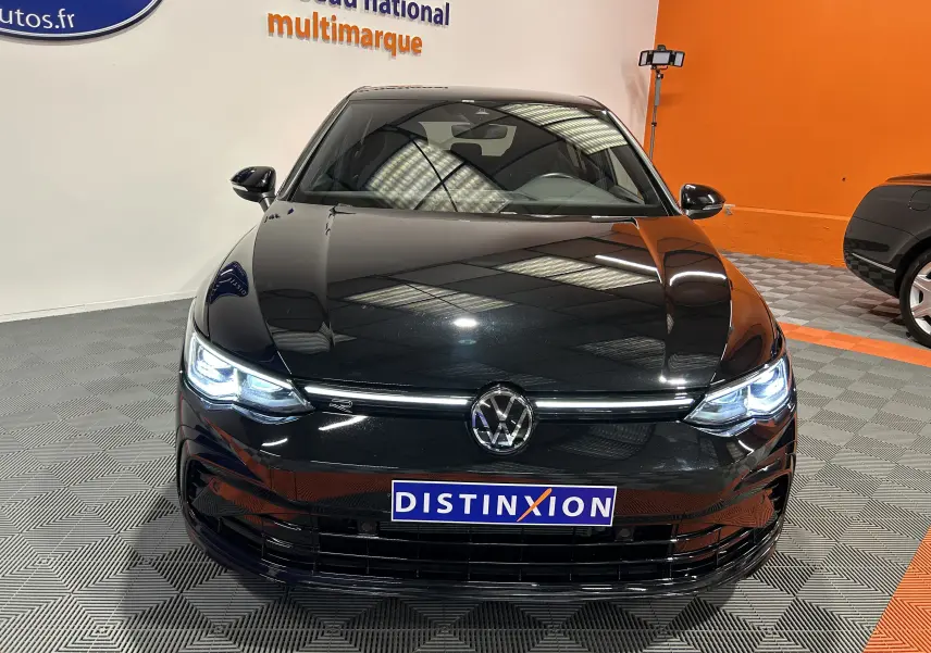 Vue avant d'une Volkswagen Golf VIII eTSI 150CH R-Line noire métal avec phares LED allumés en intérieur showroom.