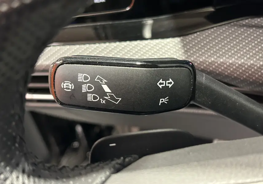Gros plan sur la commande de clignotants noire à gauche du volant dans l’habitacle d’une Volkswagen Golf VIII noire.