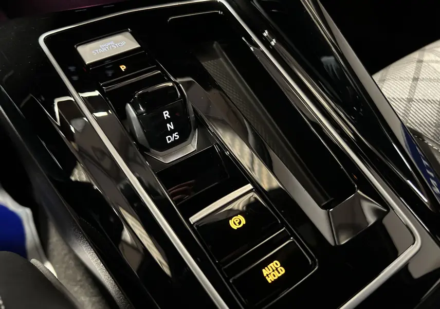 Gros plan sur la console centrale noire brillante de la Volkswagen Golf VIII eTSI avec levier de vitesse automatique et boutons éclairés.
