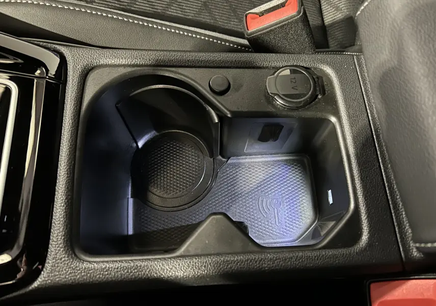 Gros plan sur le rangement central noir avec prise 12V et zone de charge sans fil dans la Volkswagen Golf VIII eTSI 2024.