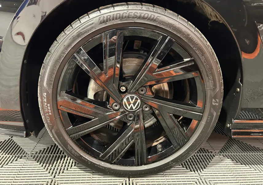 Gros plan sur la roue avant gauche noire métallisée d’une Volkswagen Golf VIII eTSI 150CH R-Line avec jante noire brillante.