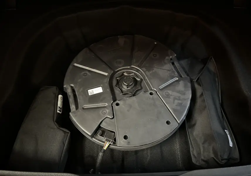 Vue rapprochée du coffre d’une Volkswagen Golf VIII eTSI 150CH R-Line noir métal, montrant la roue de secours et les accessoires de rangement.