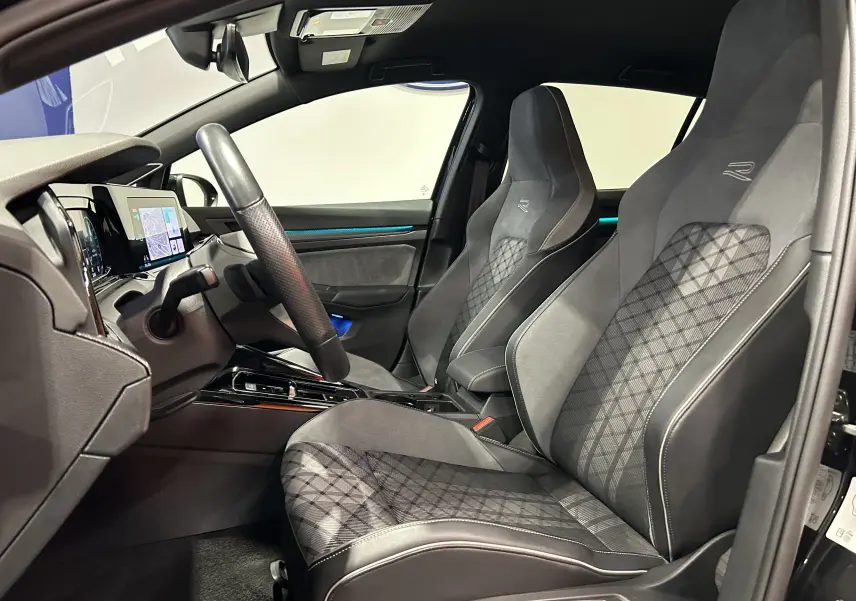 Vue intérieure côté gauche de la Volkswagen Golf VIII eTSI R-Line 2024 avec sièges sport noirs à motifs et tableau de bord digital.