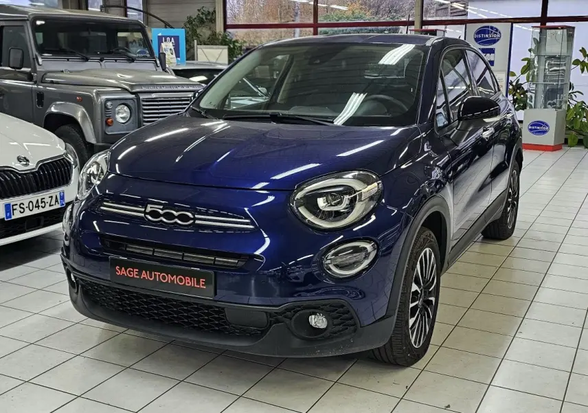 Vue 3/4 avant droite d'une FIAT 500X bleu 2024 avec logo 500 distinctif et jantes alliage en showroom.