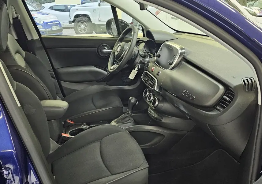 Intérieur du FIAT 500X 2024 bleu, vue côté gauche montrant sièges noirs et tableau de bord moderne avec écran tactile.