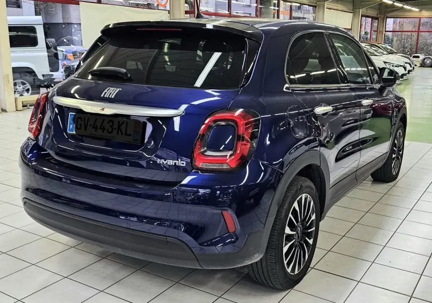 Vue 3/4 arrière droite d'un FIAT 500X bleu hybride 2024 avec feux arrière distinctifs et jantes alliage bicolores.