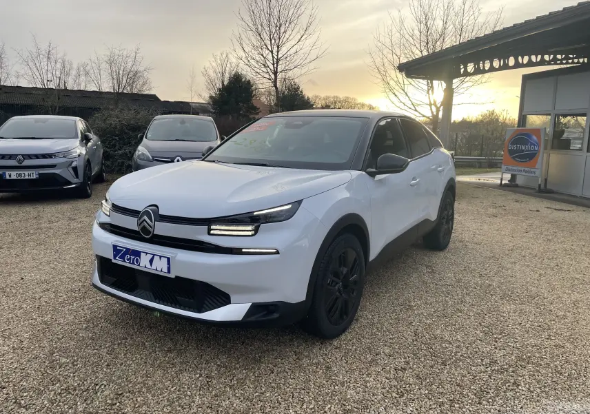 Citroën C4 hybride blanc Okenite avec toit noir Perla, vue 3/4 avant droit sur parking extérieur au coucher du soleil.