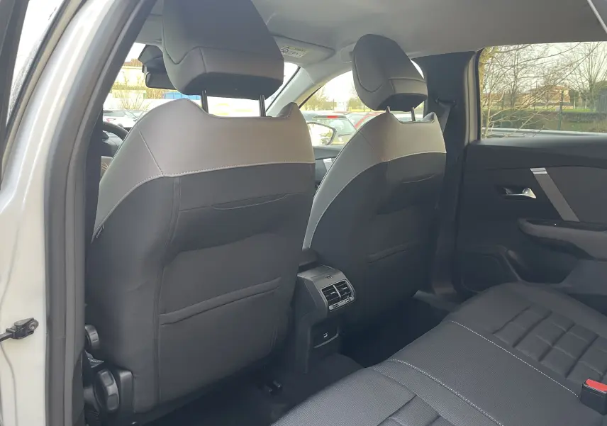 Vue intérieure arrière côté gauche montrant les sièges avant en tissu noir avec surpiqûres et les aérateurs centraux du Citroën C4 blanc.