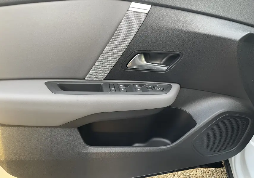 Gros plan sur la porte intérieure côté gauche de la Citroën C4 blanche, avec garniture noire et grise et commandes de vitres.