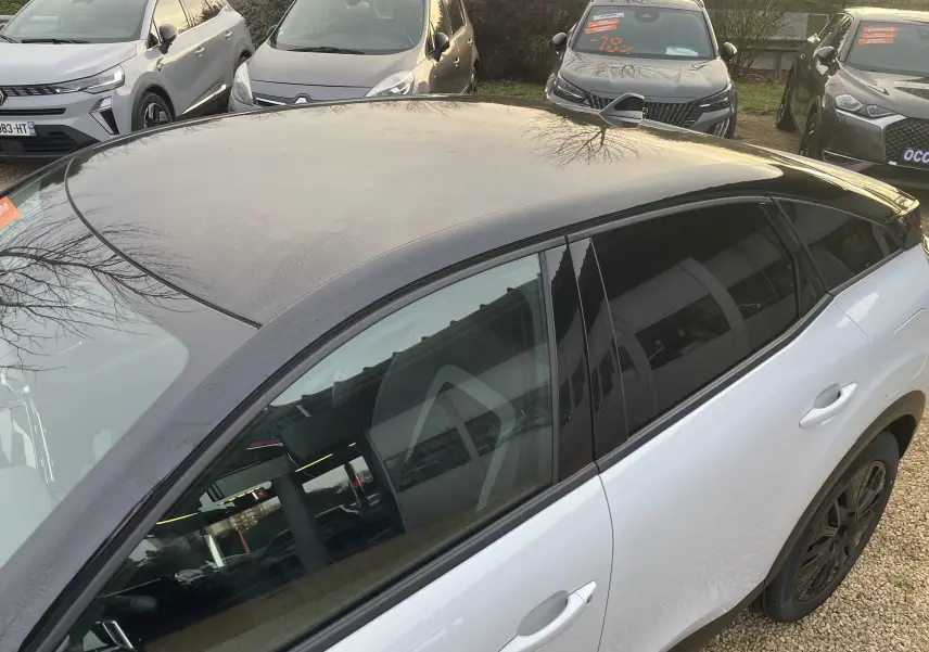 Vue 3/4 arrière côté droit de la Citroën C4 blanche Okenite avec toit noir Perla et jantes noires, en extérieur.