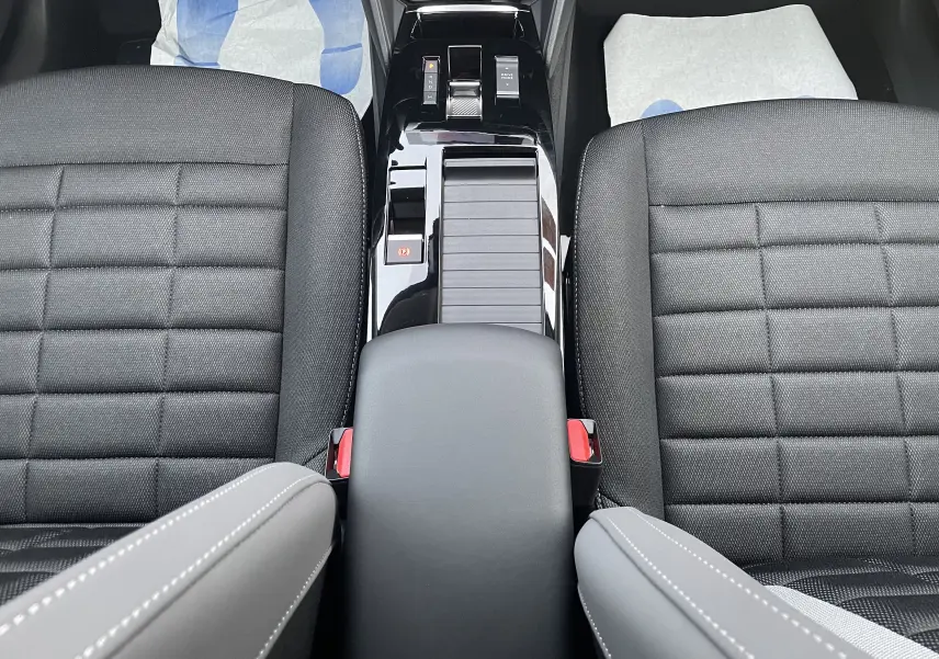 Vue plongeante sur la console centrale noire brillante et les sièges avant en tissu noir de la Citroën C4 hybride 2025.