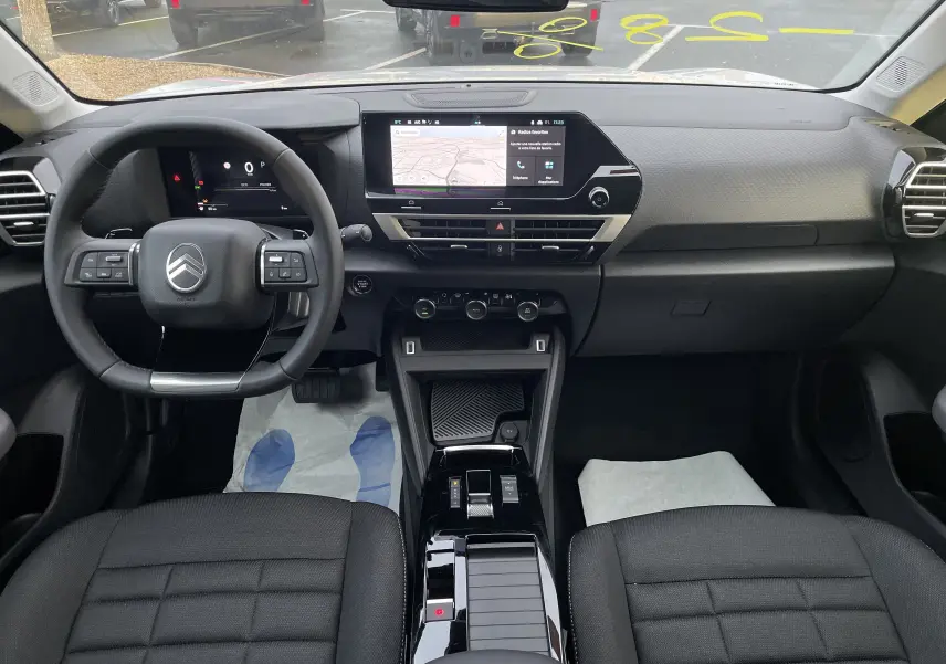 Vue intérieure avant du Citroën C4 2025, tableau de bord noir avec écran tactile central et volant multifonction.