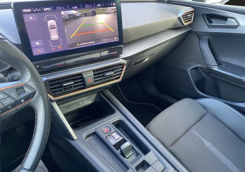 Vue intérieure côté passager de la CUPRA Leon noire 2023, avec écran tactile affichant la caméra de recul et volant perforé.