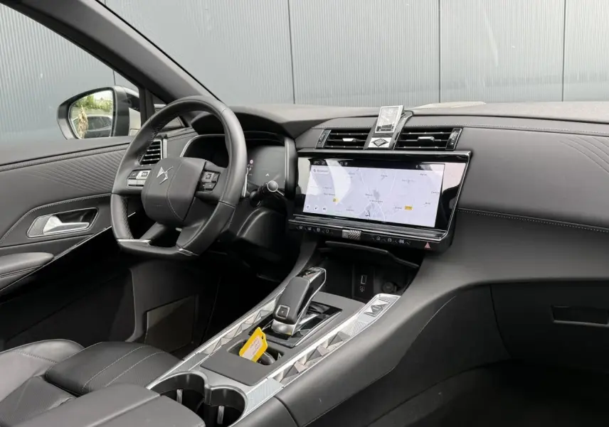 Intérieur DS7 2025 vu côté conducteur, tableau de bord noir avec écran tactile large et console centrale argentée.