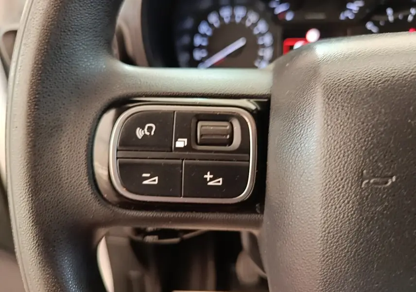 Gros plan sur les commandes multifonctions noires du volant de la Citroën Berlingo blanc, avec tableau de bord flou en arrière-plan.
