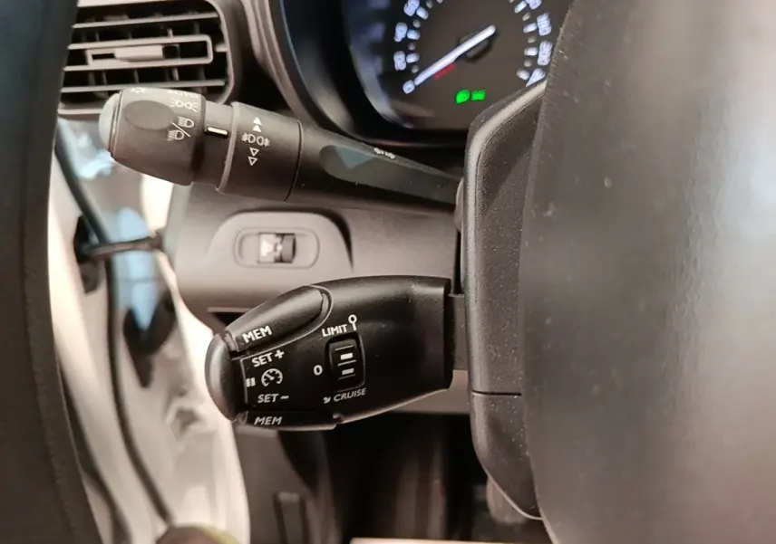 Gros plan sur le volant et commandes de régulateur de vitesse du Citroën Berlingo blanc, tableau de bord en arrière-plan.